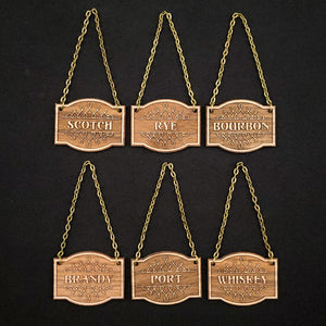 Laser engraved decanter tags made from walnut adds a beautiful vintage touch to your bar; the options displayed include "Scotch", "Rye", "Bourbon", "Brandy", "Port", and "Whiskey."