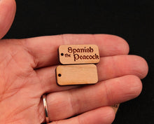 Load image into Gallery viewer, 1&quot; x .5&quot; custom laser engraved tags cut from hardwoods. Tags can be used for product branding, packaging, or gift bags. Shown against a hand for sizing.
